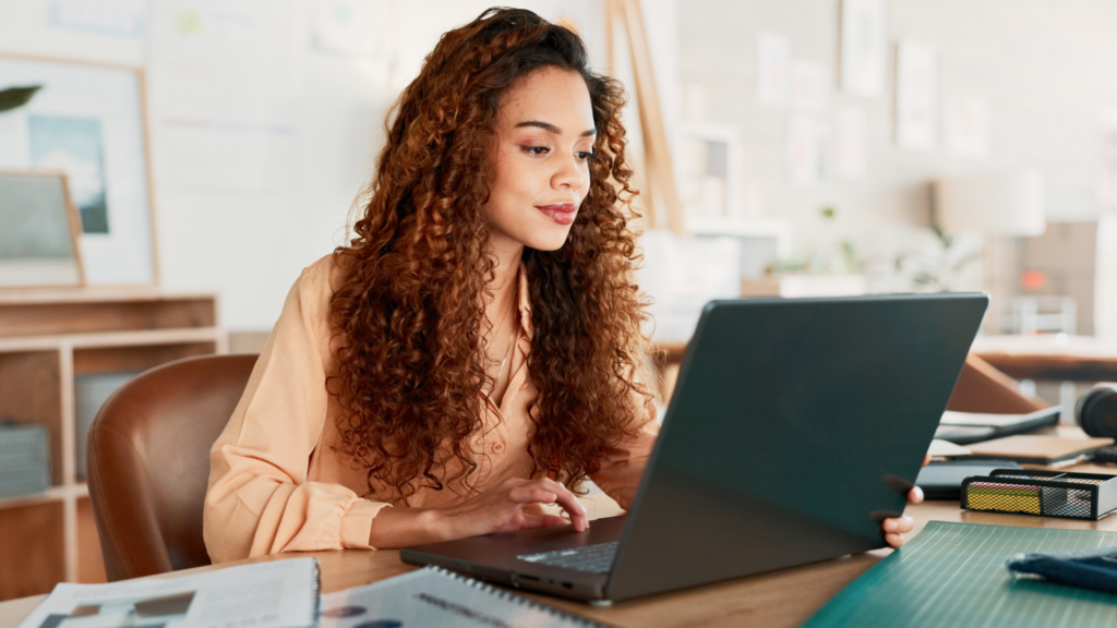 9 common Pinterest mistakes Etsy sellers should avoid A woman with curly hair sits at a desk, focused on her laptop while working.
