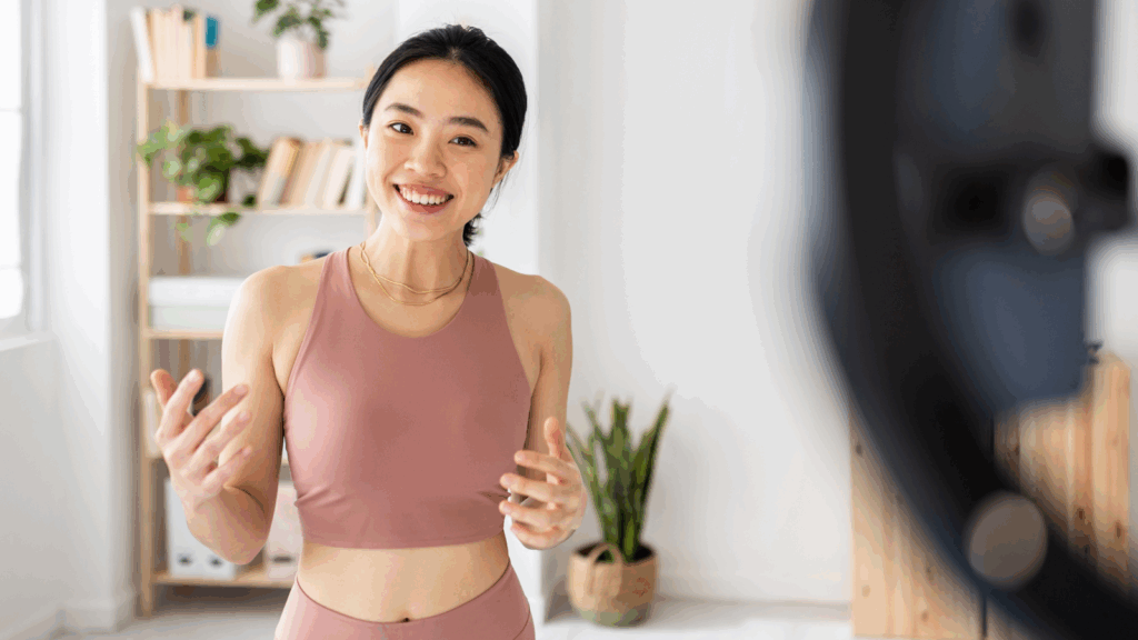 Leverage social media How to start a clothing brand A smiling woman dressed in athletic apparel is recording herself using a mobile phone.